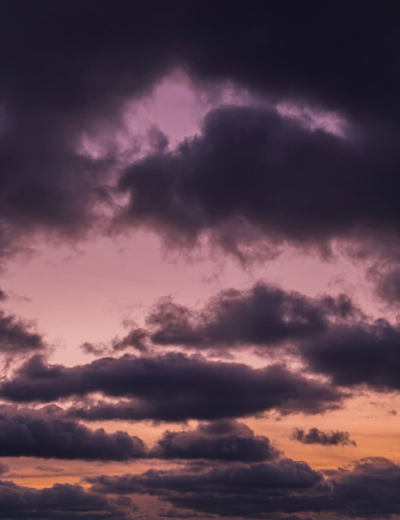 Dramatic dusk sky with purple and grey clouds over glowing lavender and gold gradient background Wallpaper