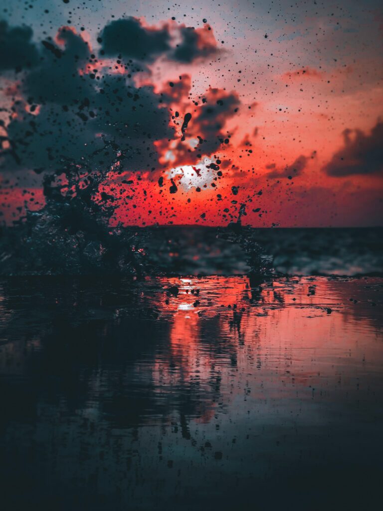Dynamic water splash over reflective sea at dusk with deep blue and fiery orange hues wallpaper