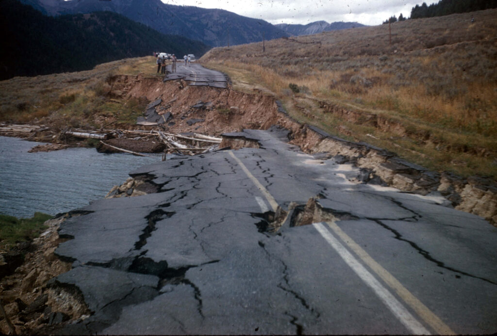 Dramatic earthquake aftermath with cracked asphalt road landslide debris rugged mountains cloudy sky Wallpaper