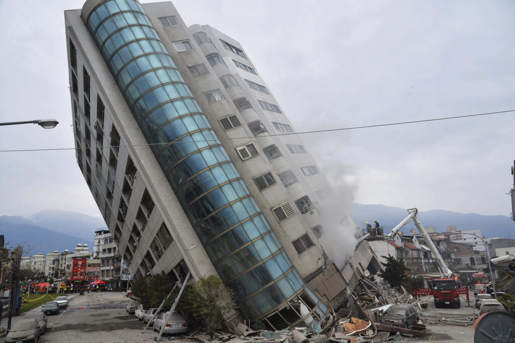 Tilted modern building after earthquake surrounded by rescue workers fire trucks and debris background Wallpaper