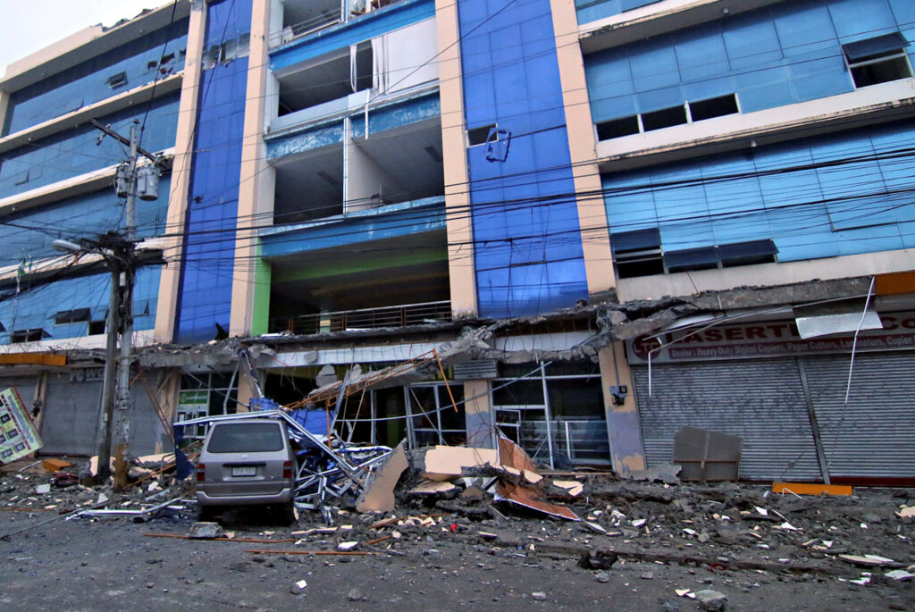 Earthquake aftermath showing damaged building with collapsed walls shattered glass and debris urban disaster Wallpaper