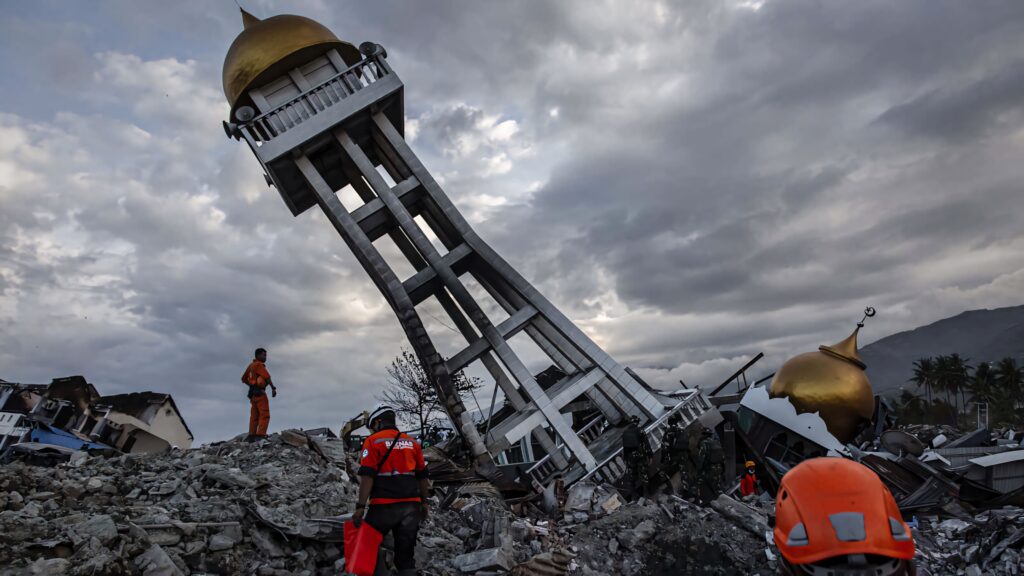 Rescue workers navigate earthquake rubble beneath toppled mosque tower under stormy skies wallpaper
