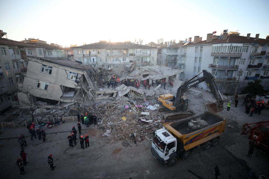 Earthquake disaster scene with collapsed buildings rescue workers and heavy machinery in muted tones Wallpaper