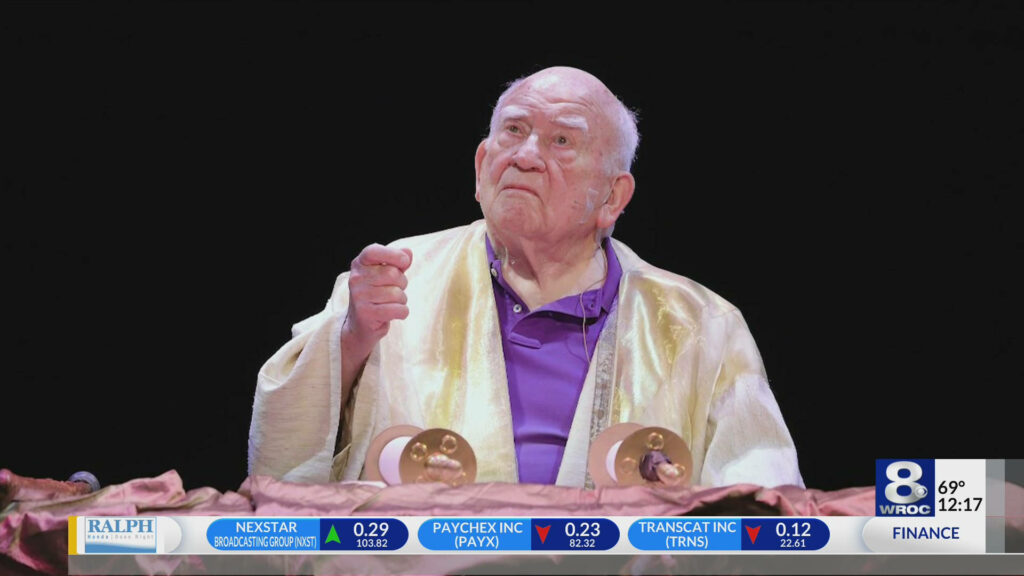 Ed Asner in gold robe and purple shirt on TV show with dramatic cinematic lighting wallpaper background