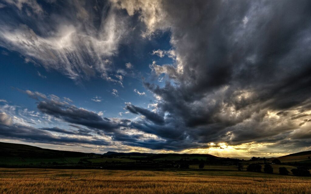 Dramatic evening sky with swirling clouds over golden rye field calm storm wallpaper background