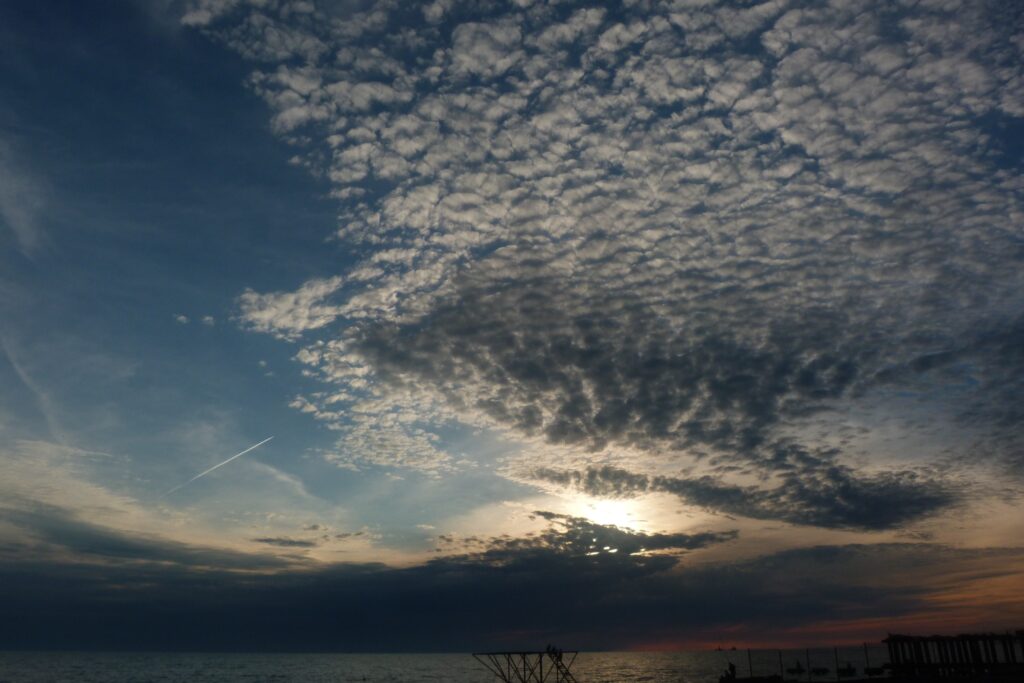 Dramatic evening sky over sea with textured clouds and sun casting warm cool tones reflection Wallpaper