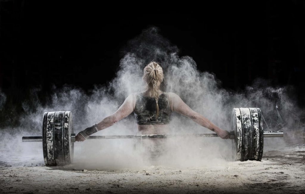 Female athlete lifting heavy barbell with chalk dust explosion intense weightlifting workout Wallpaper