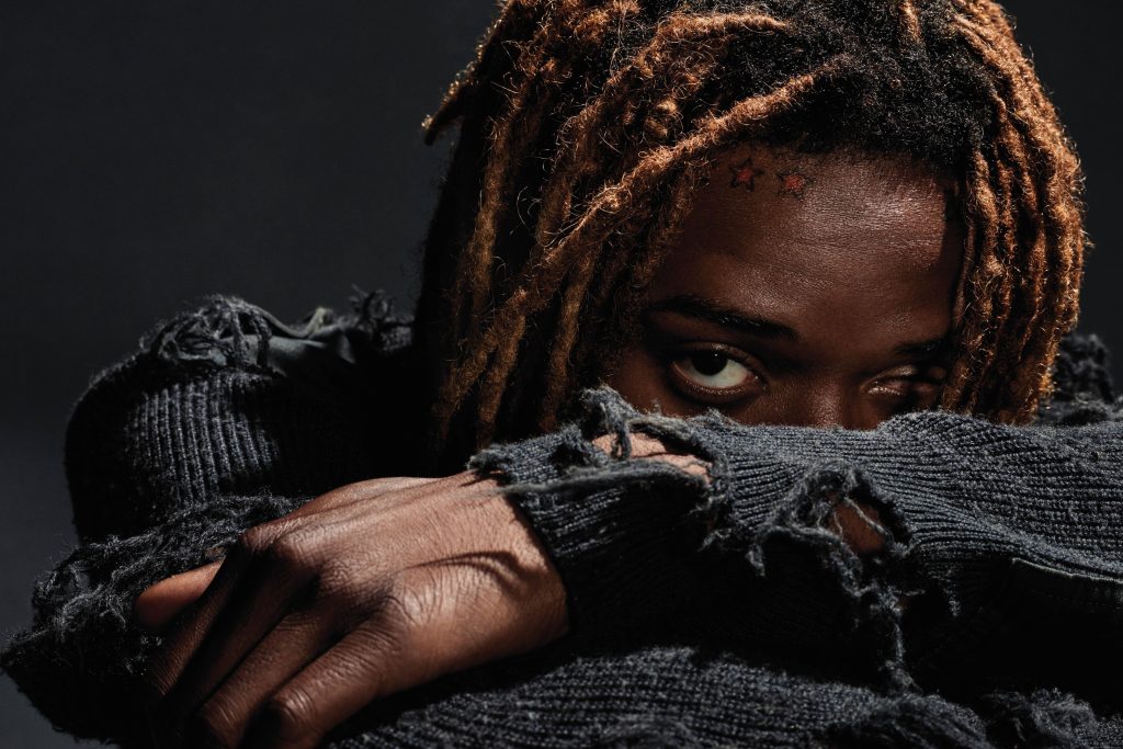 Dramatic portrait of rapper Fetty Wap with dreadlocks star tattoos dark sweater studio lighting Wallpaper