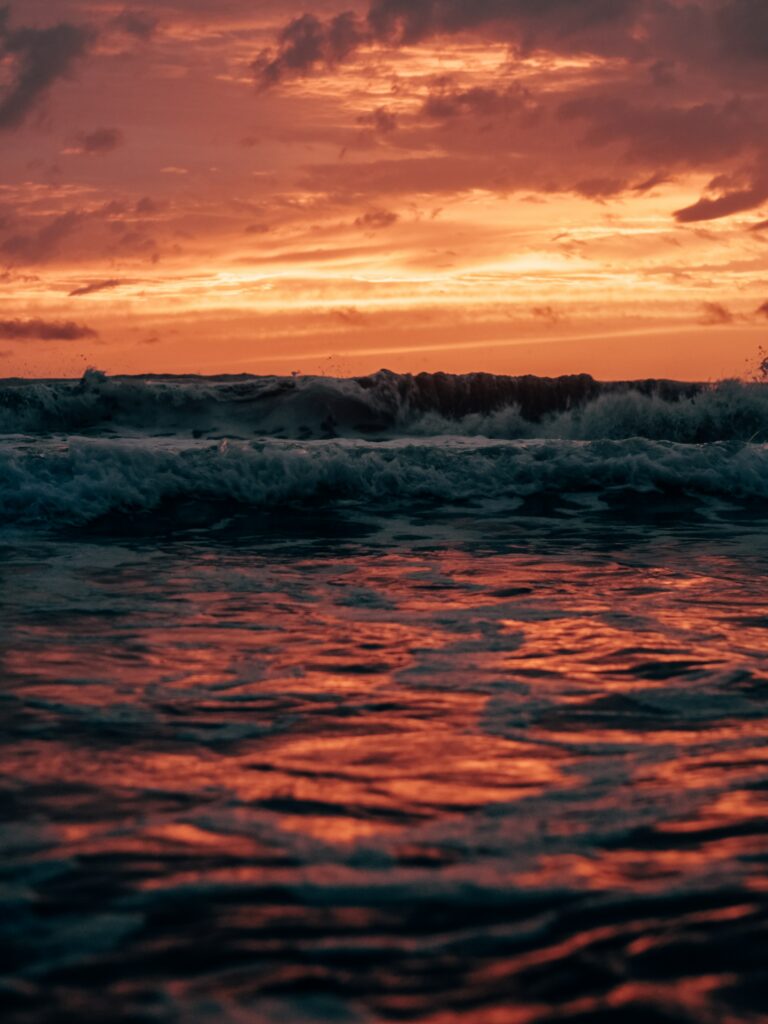 Dramatic dusk seascape with fiery orange and red sunset reflecting on rolling ocean waves wallpaper