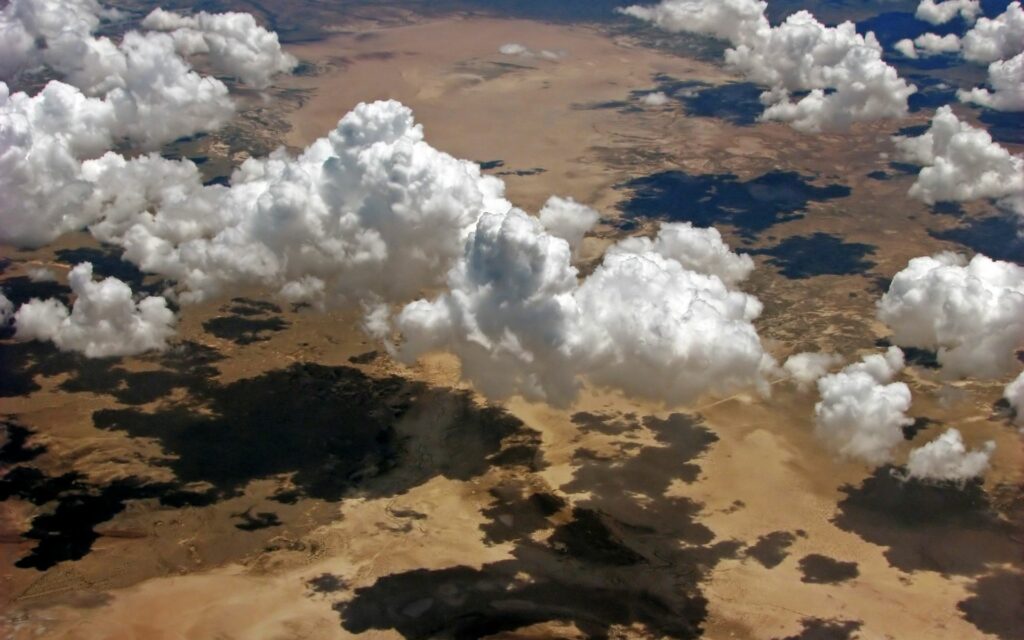 Aerial view of sunlit desert with fluffy clouds casting dramatic shadows over landscape Wallpaper
