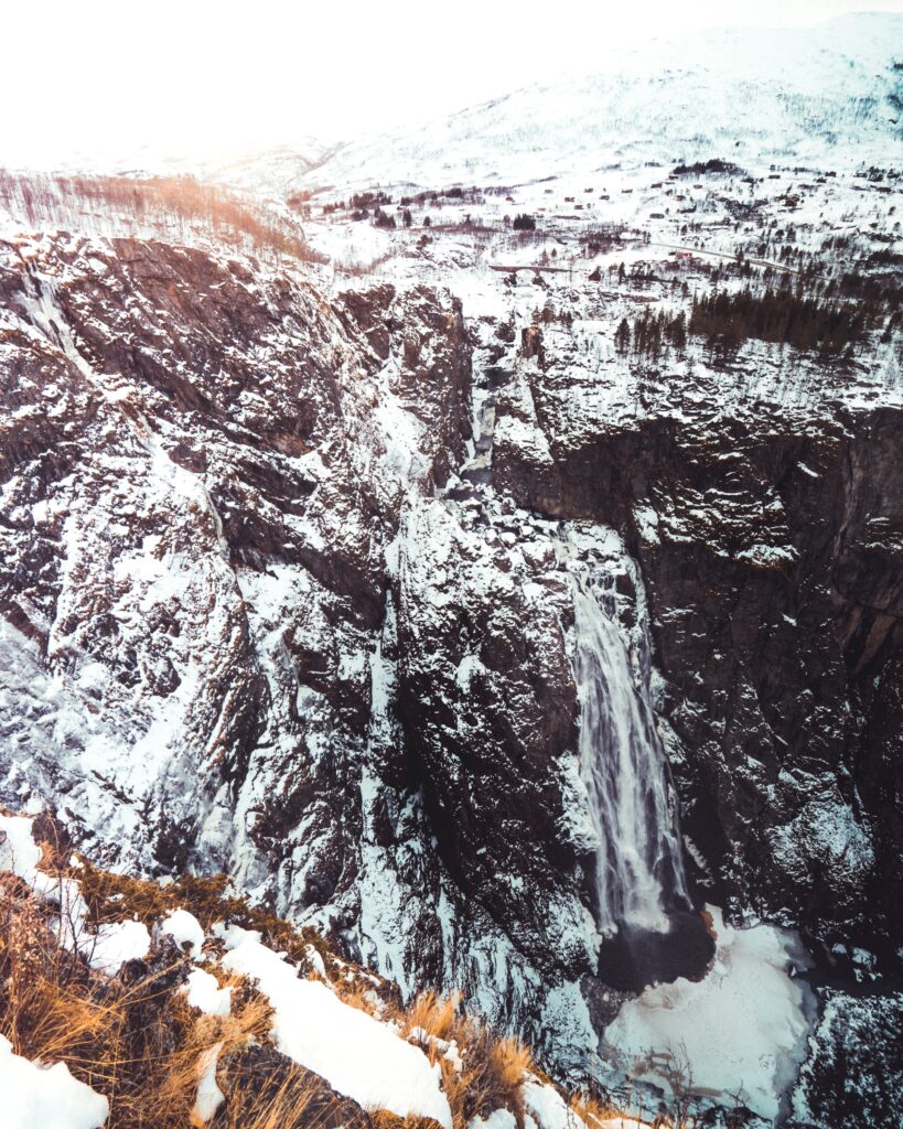 Frozen waterfall cascading down snow-covered cliff in dramatic winter landscape wallpaper background