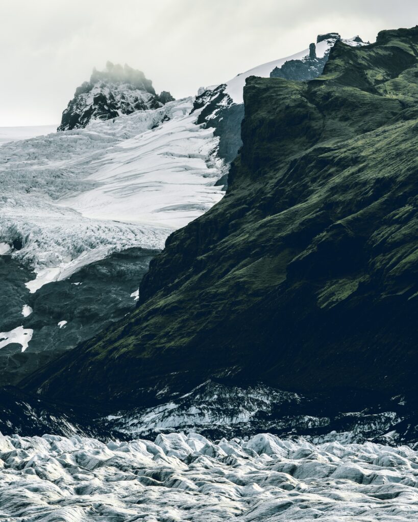 Glacier covered mountains with rugged rocks lush green slopes and misty sky landscape wallpaper