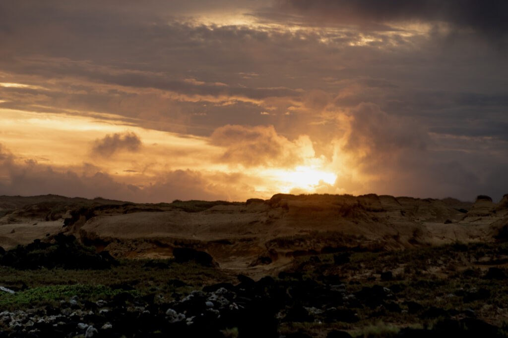 Dramatic sunset with golden light through clouds over rugged stones and sandy terrain wallpaper
