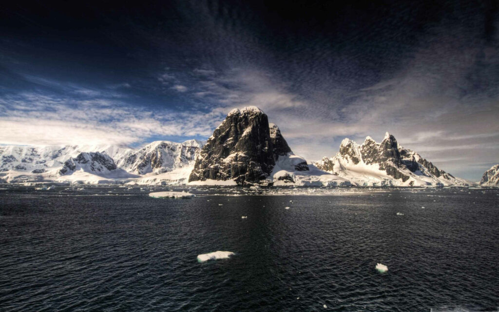 Graphite mountain rising from icy Antarctic landscape with snow peaks and cold ocean under sky Wallpaper