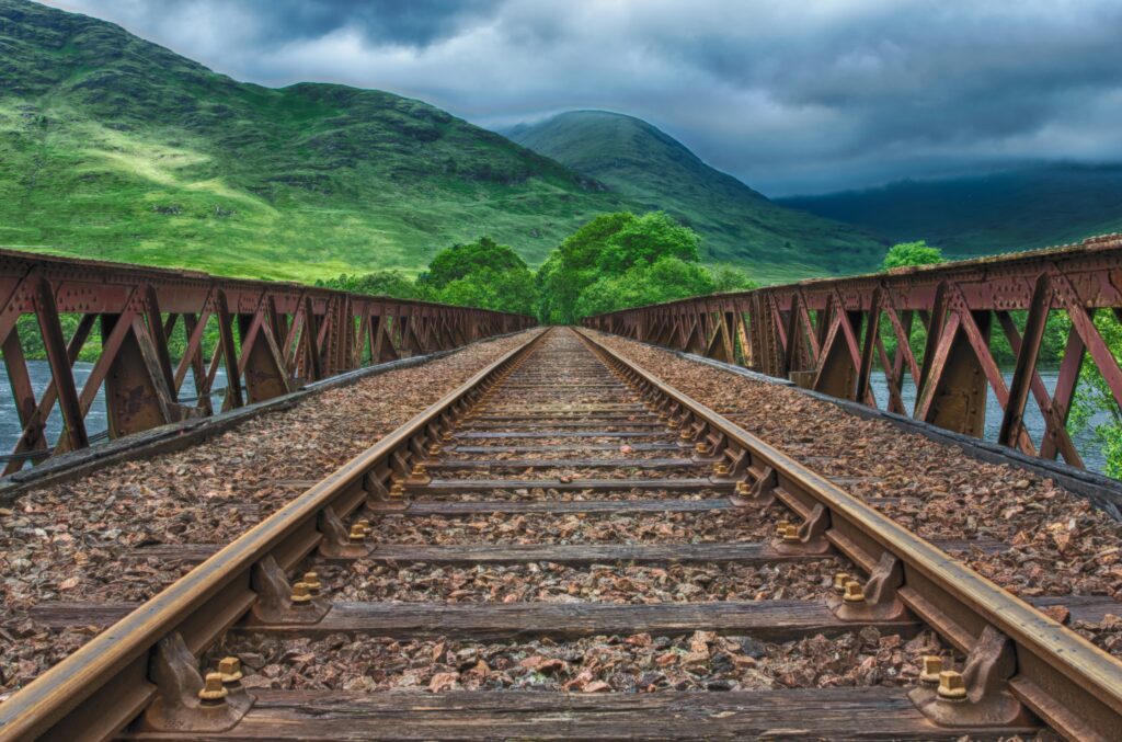 HDR railway tracks on rustic bridge with green mountains and cloudy sky wallpaper background