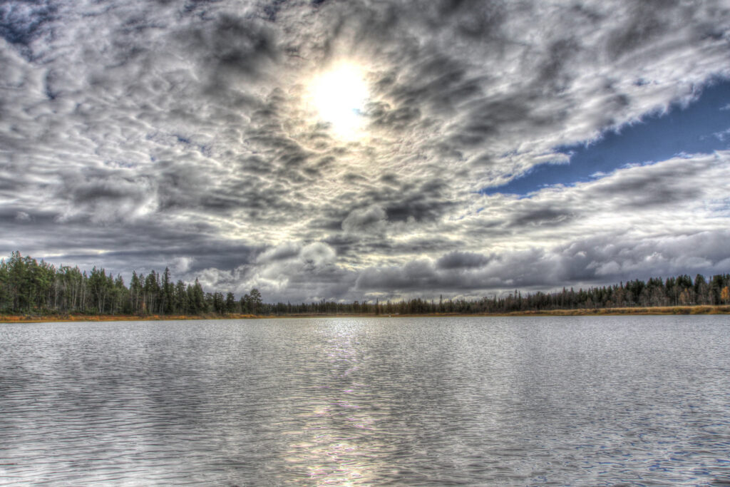 Dramatic HDR lake landscape with dense forest sunlight breaking through clouds reflecting water Wallpaper