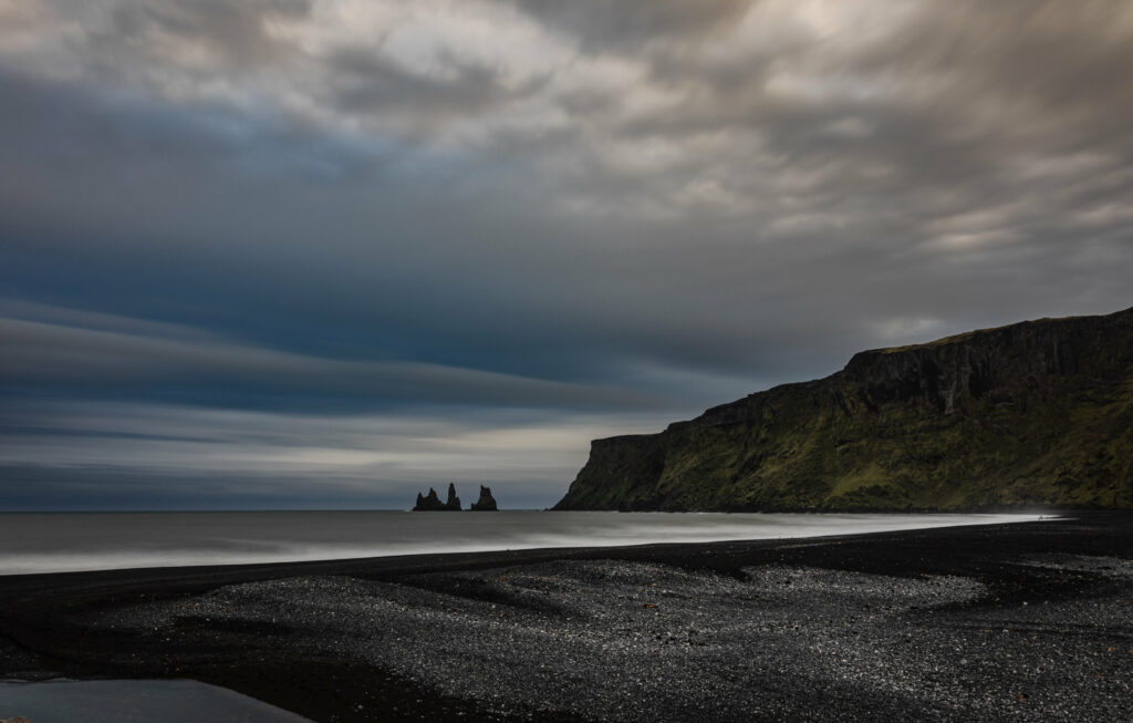 Dramatic Iceland coast with rugged cliffs black sand beach sea stacks and moody cloudy sky wallpaper