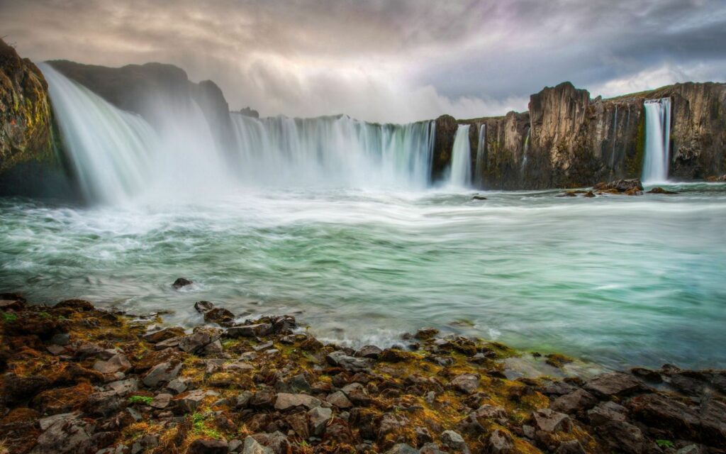 Icelandic waterfall cascading over rugged rocks into swirling streams with misty wild landscape Wallpaper
