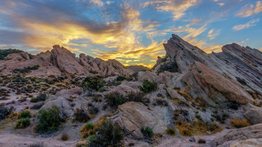 Jagged rock formations under vibrant sky with wispy clouds and green shrubs natural wallpaper background