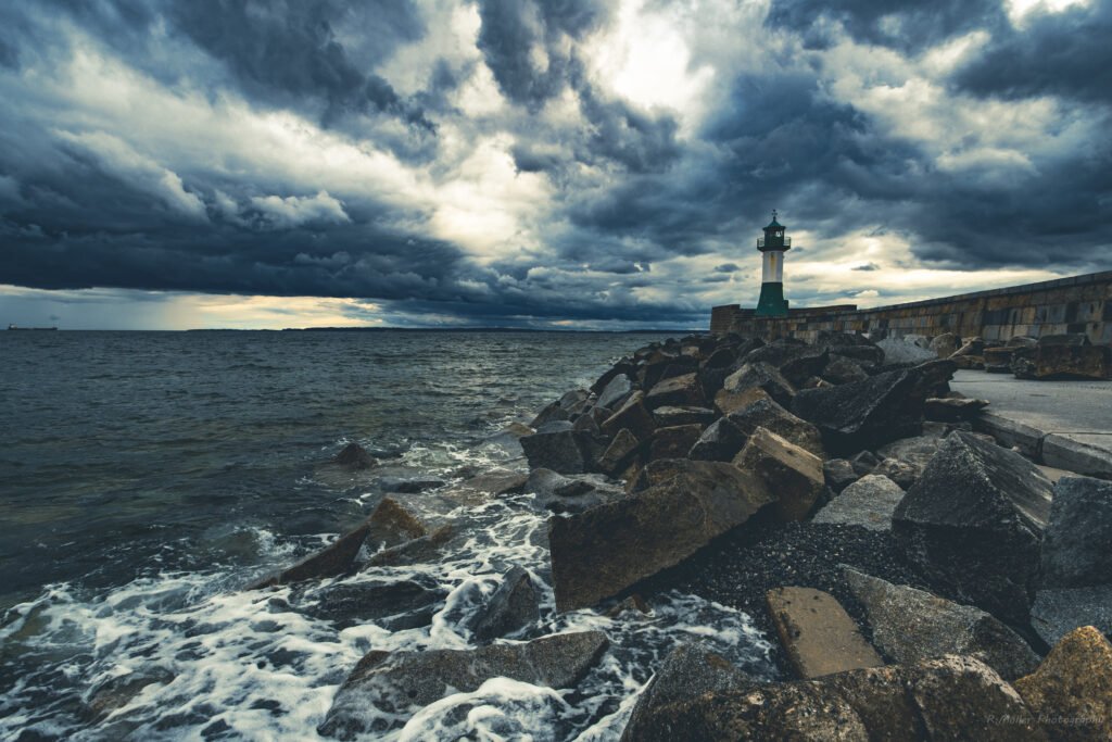Dramatic seascape lighthouse on rugged stone coast with crashing waves and moody cloudy sky Wallpaper