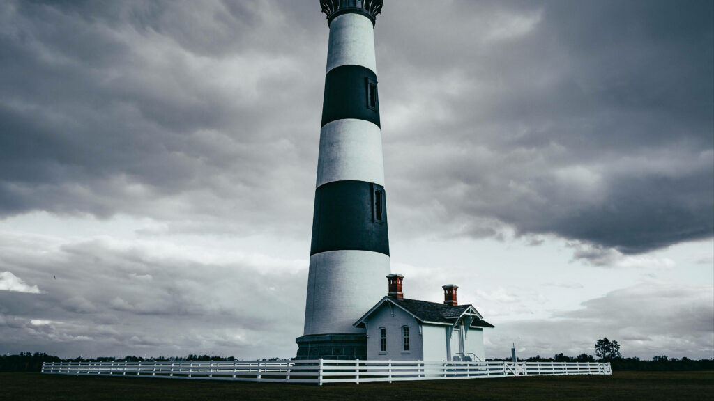 Majestic Lighthouse Against Stormy Sky: A Striking Coastal Scene Wallpaper