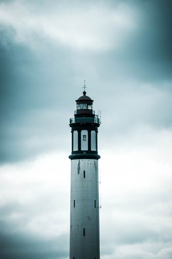 Lighthouse with white exterior and dark accents under dramatic cloudy sky by the sea wallpaper