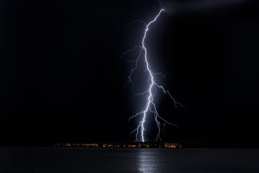 Vivid lightning bolt splits night sky over dark sea illuminating horizon with electric light wallpaper