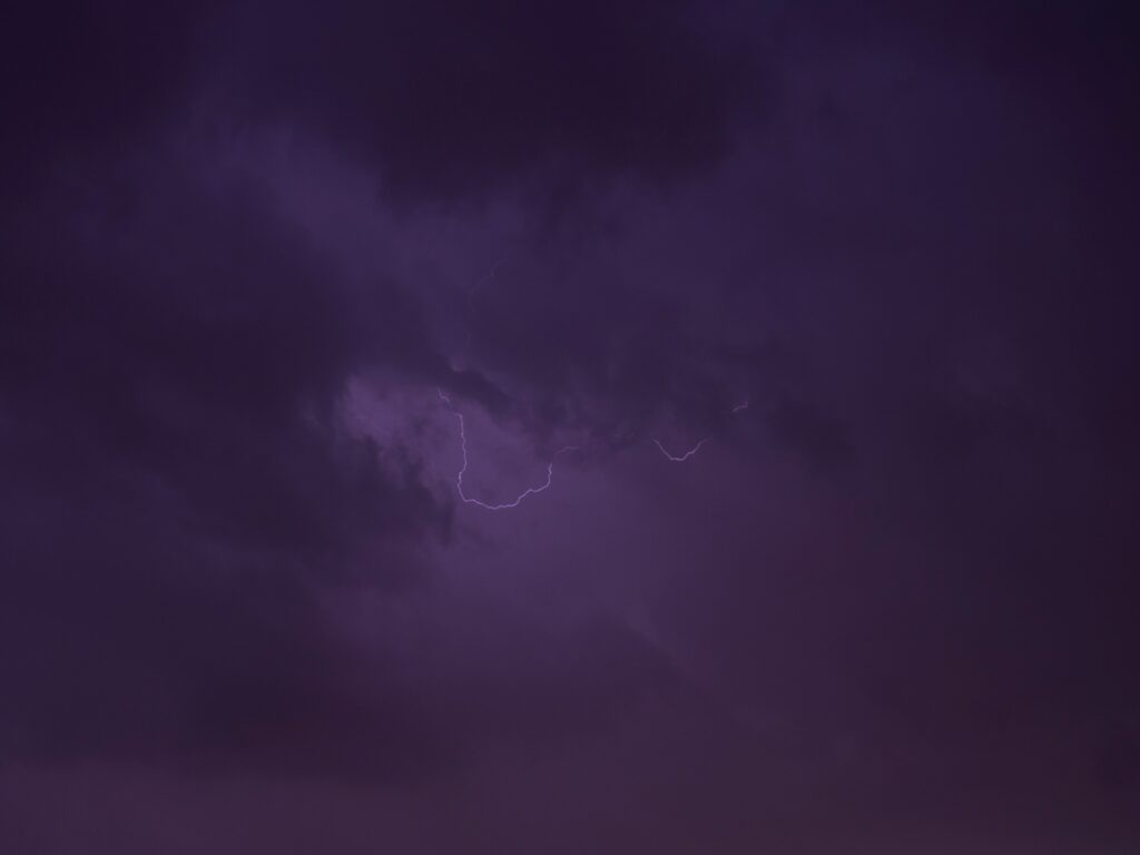 Dramatic vivid lightning bolt striking through dark stormy clouds with deep purple sky wallpaper