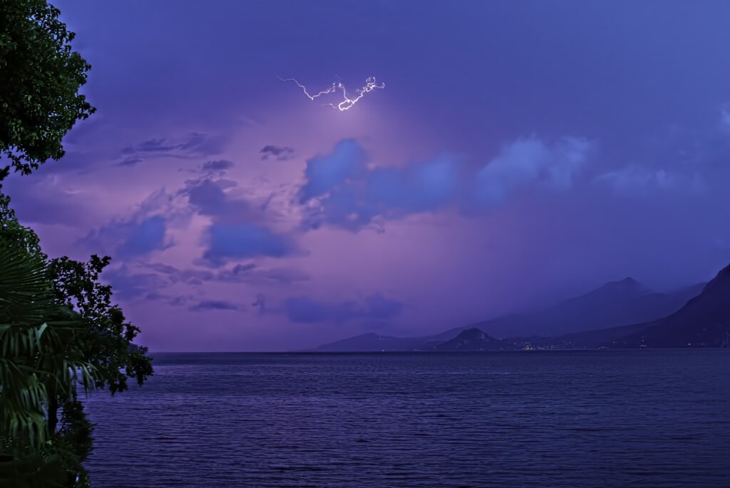 Calm sea under vivid lightning with distant mountains lush greenery dramatic sky wallpaper