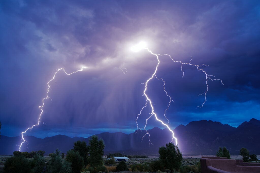 Dramatic thunderstorm with vivid lightning bolts over mountains and trees at night wallpaper