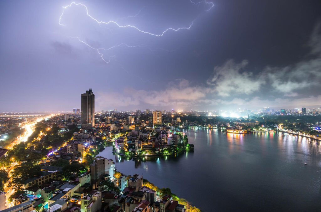 Lightning storm lights up Vietnam cityscape at night with glowing city lights reflecting river Wallpaper