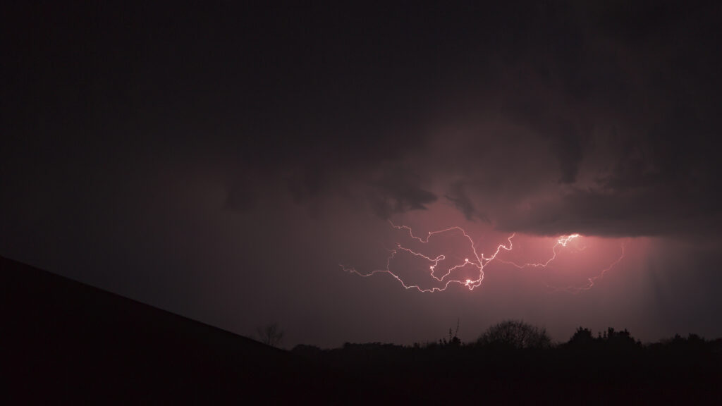 Dramatic lightning storm with pink glowing clouds in a moody night sky wallpaper background