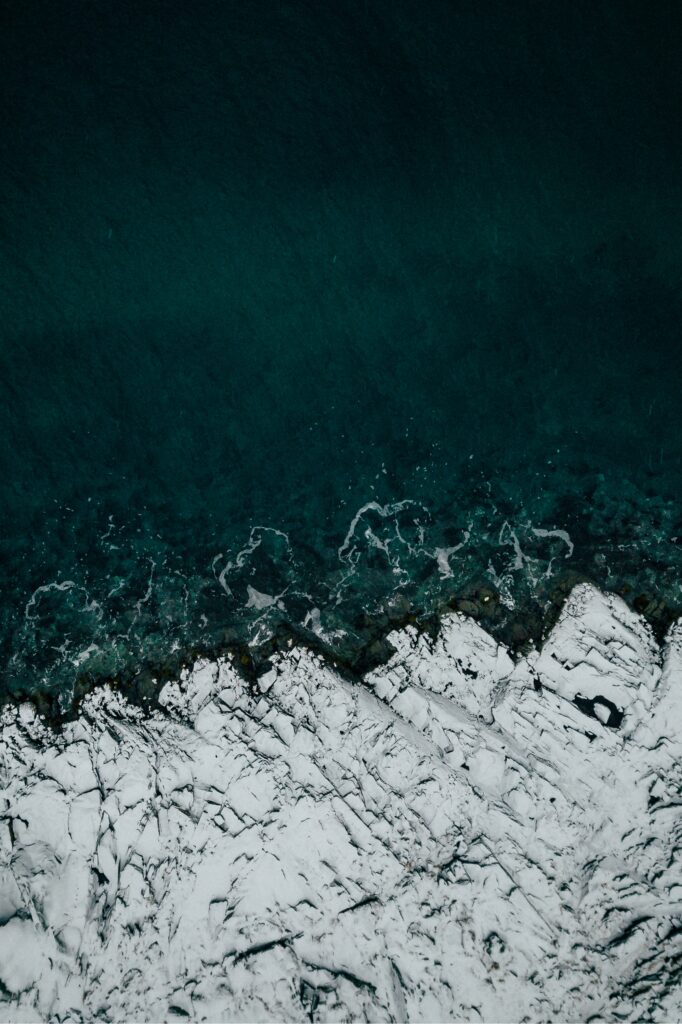 Aerial view of Lofoten Islands coastline with turquoise sea and snow-covered rugged rocks Wallpaper