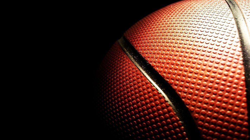 Macro close-up of textured orange basketball surface with black seam on dark background wallpaper