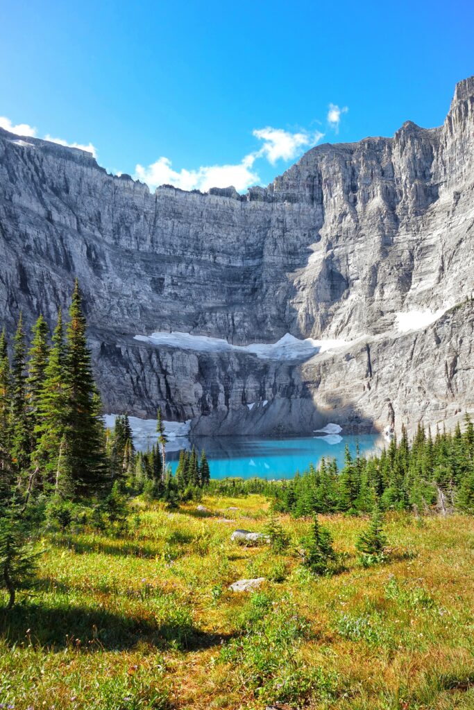 Dramatic mountain cliff over clear blue lake with green trees and bright sky landscape wallpaper