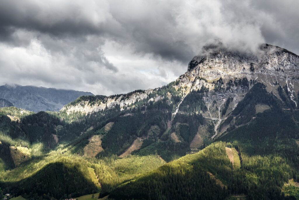 Dramatic mountain cliff with lush green grass under sunlight breaking through cloudy sky wallpaper