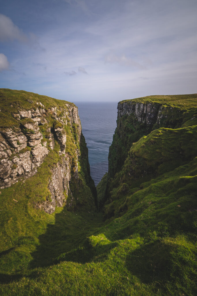 Rugged green mountain cliffs overlooking deep blue sea under soft clouded sky wallpaper background