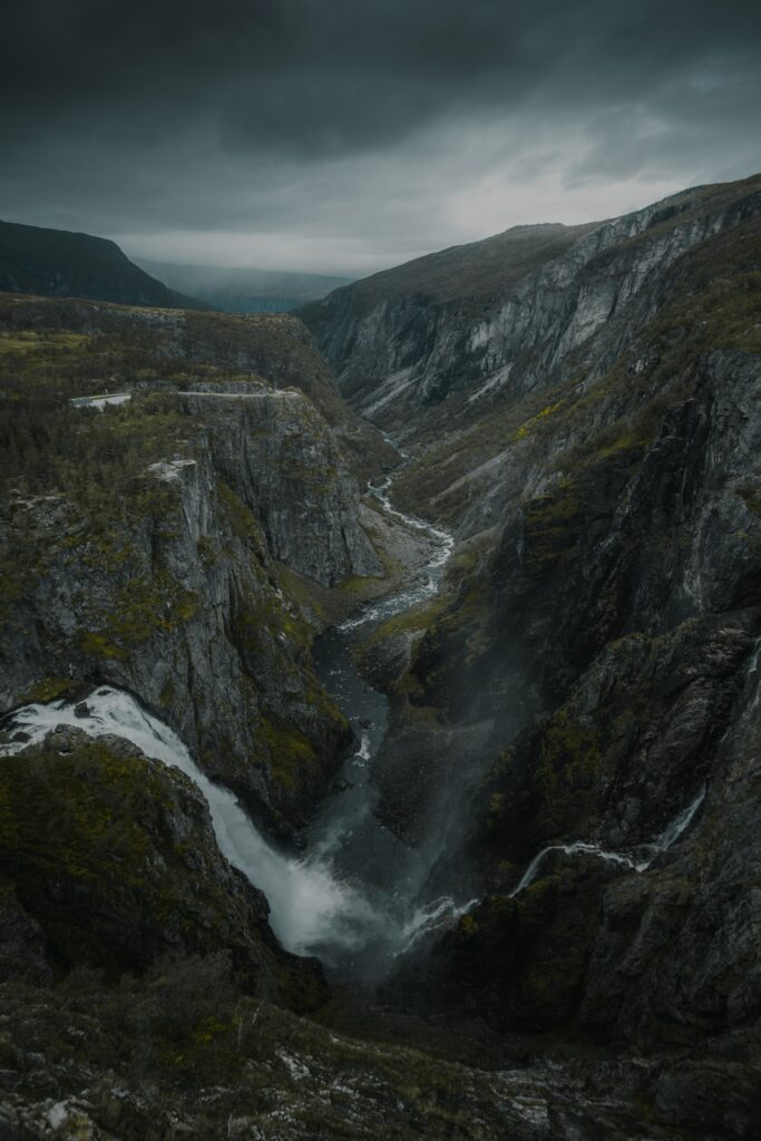 Dramatic gorge with rocky cliffs winding river and waterfall under moody overcast sky wallpaper