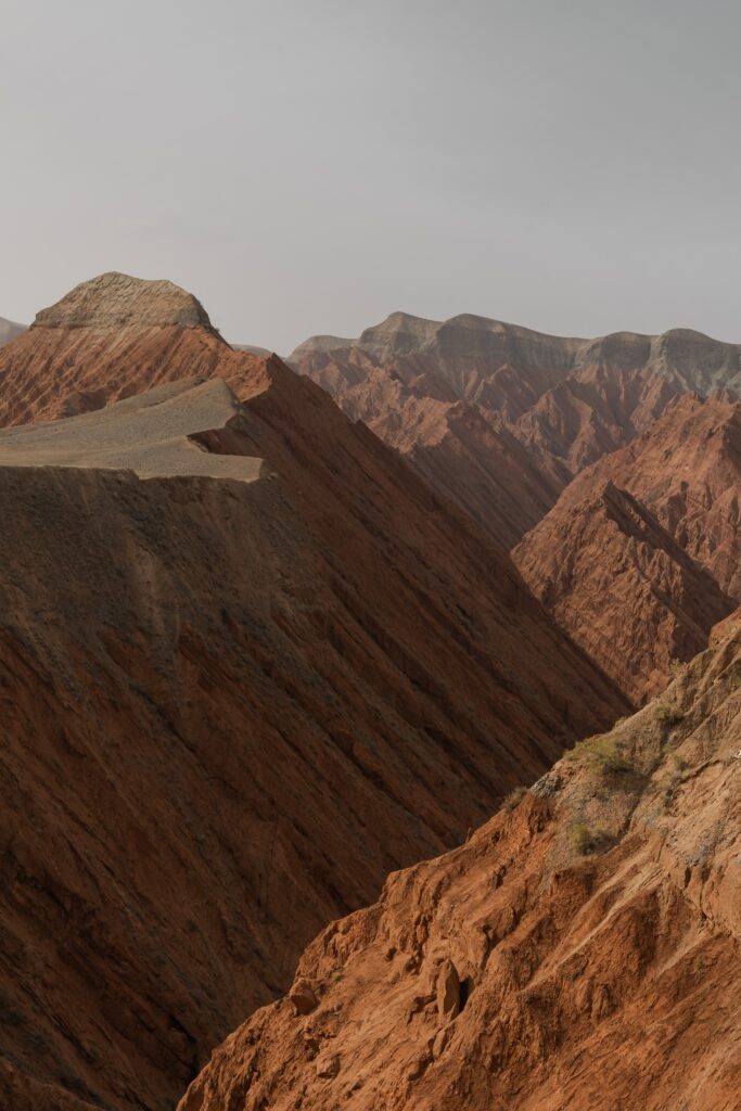 Dramatic mountain landscape with rugged brown slopes and layered peaks under soft sky wallpaper