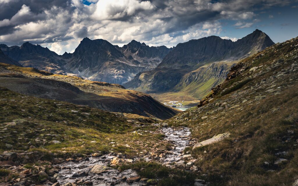 Dramatic mountain landscape with rugged peaks rocky stream lush green valley and dynamic skies Wallpaper