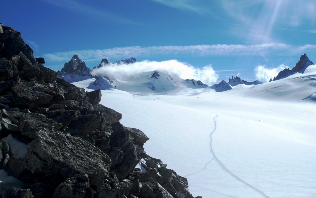 Dramatic mountain landscape with rugged stones snow avalanche and bright sun under clear sky Wallpaper