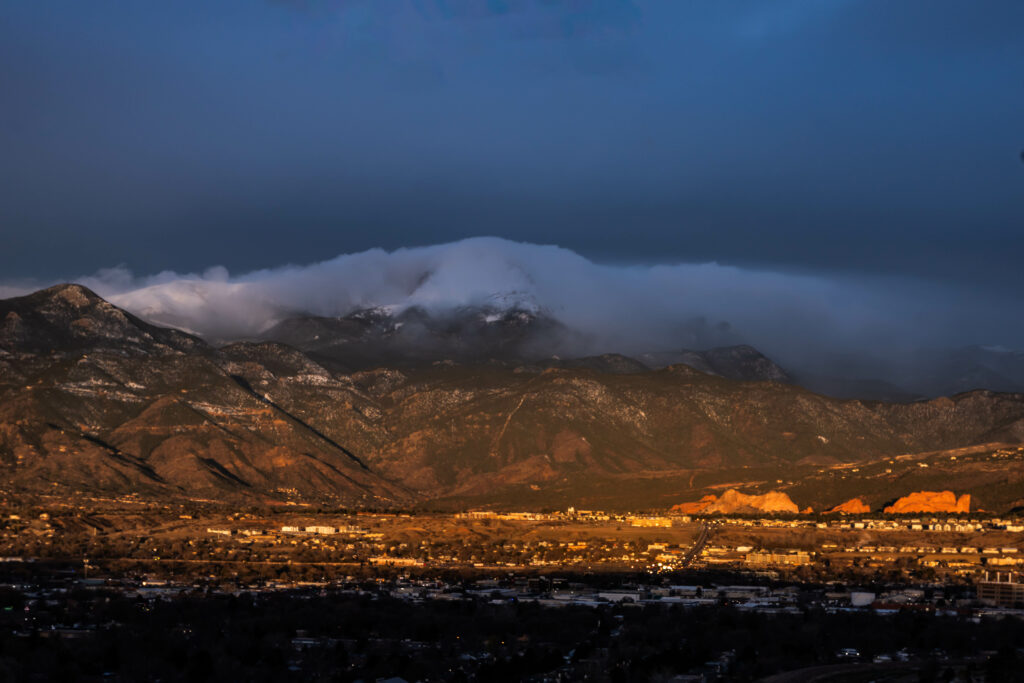 Dramatic mountain landscape with sunlit valley and dark peaks under thick cloud cover wallpaper