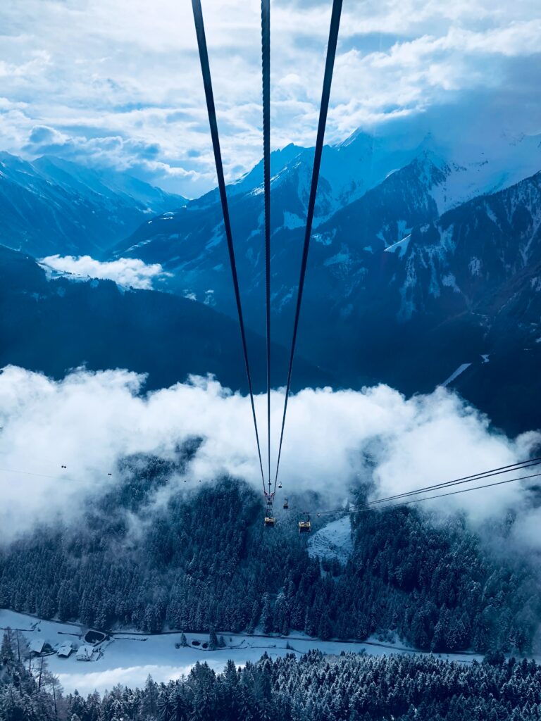 Dramatic mountain landscape with cable car above snow-dusted trees and misty blue peaks wallpaper