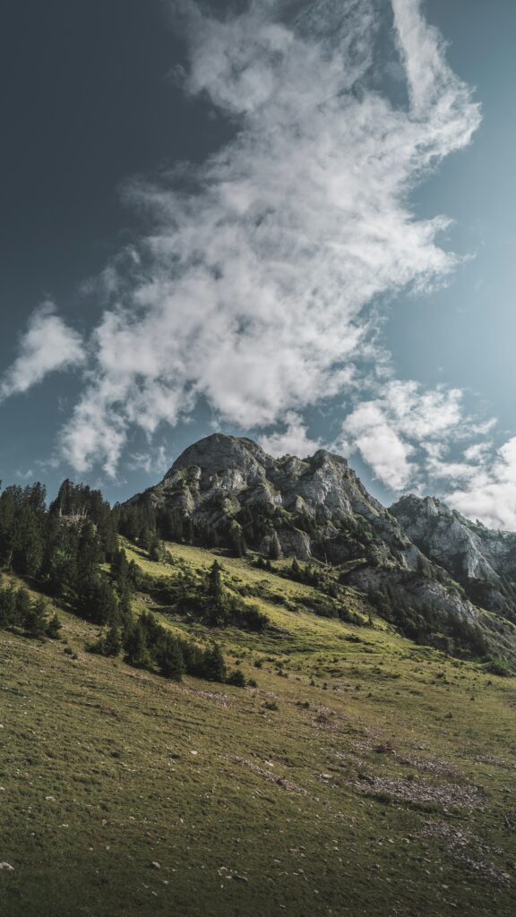 Dramatic mountain landscape with rugged rocks lush green foothills and wispy clouds in blue sky Wallpaper