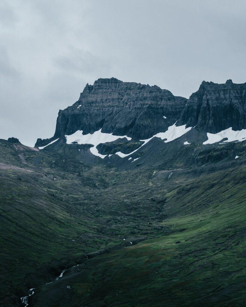 Dramatic mountain landscape with rugged rocks snow patches winding river and lush green valleys Wallpaper