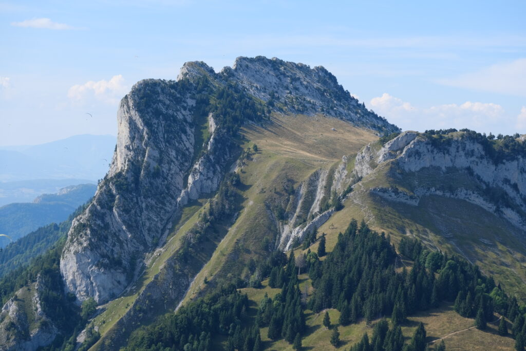 Dramatic mountain landscape with rugged rocky slopes and green trees under clear blue sky wallpaper
