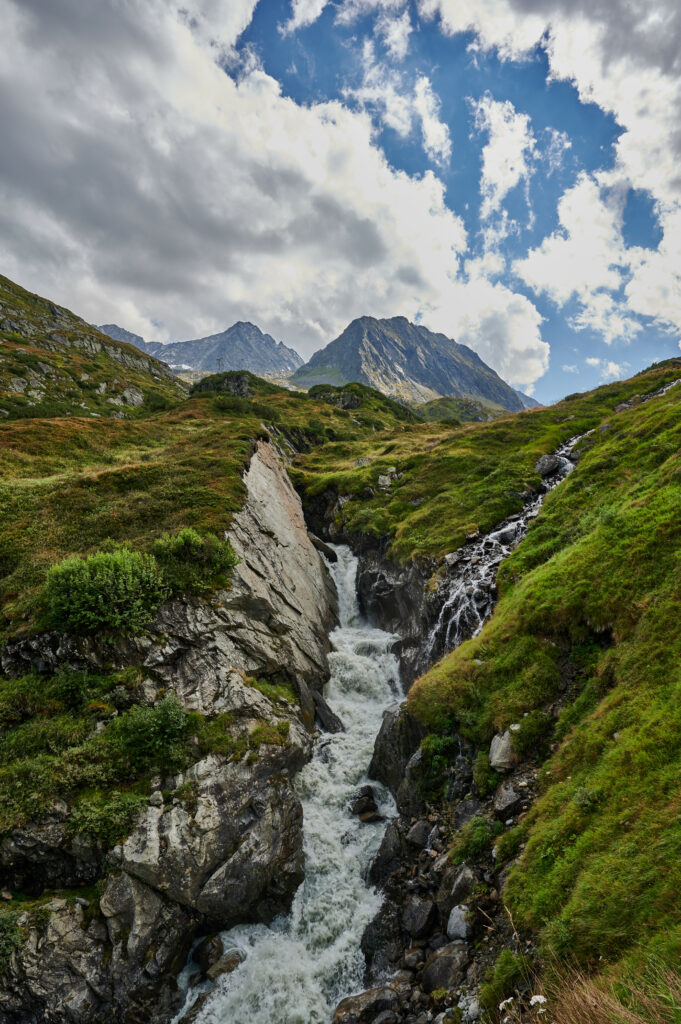 Dramatic mountain landscape with rushing stream over stones and lush green grass background Wallpaper