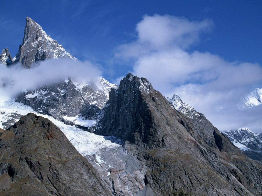 Dramatic mountain landscape with sharp gray white peaks under vivid blue sky and wispy clouds Wallpaper