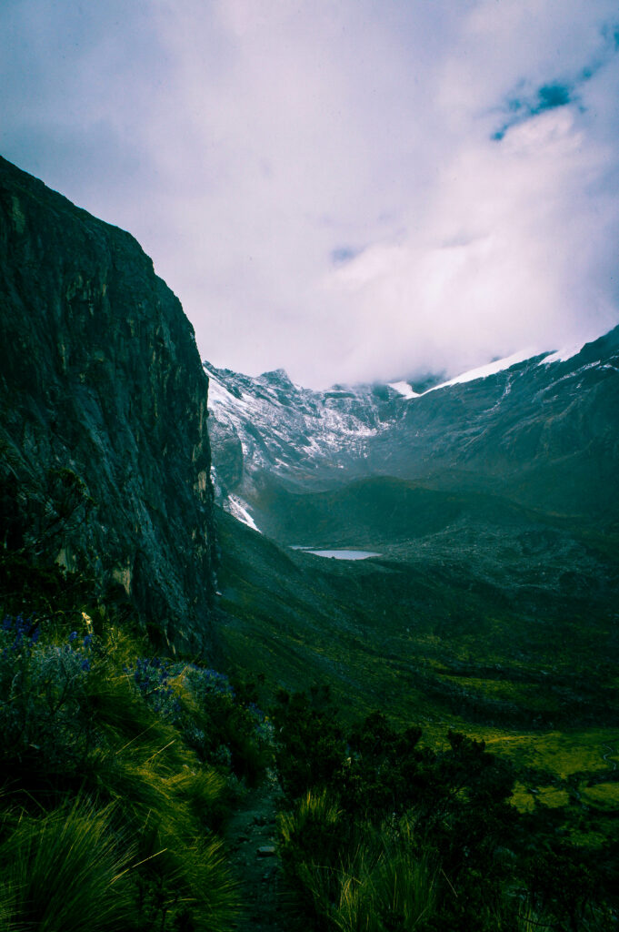 Dramatic mountain landscape with rocky cliffs snow patches grassy meadows and misty cloudy sky Wallpaper