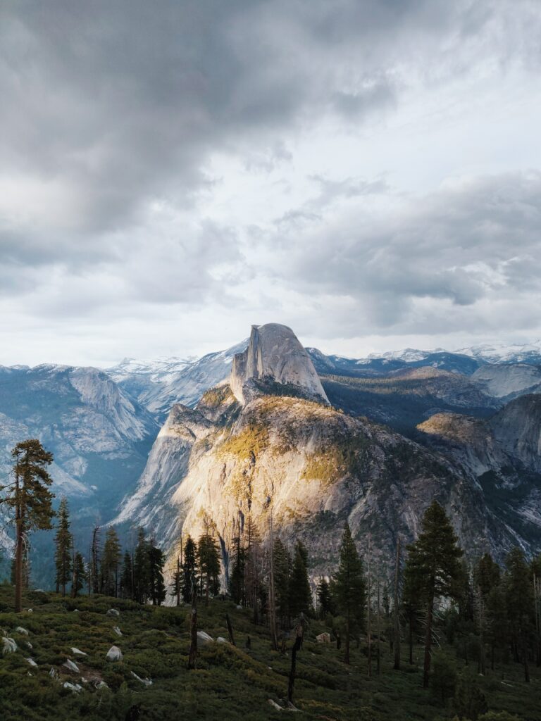 Dramatic mountain landscape with towering cliffs lush green forest and moody sky wallpaper background